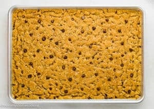 A rectangular baking pan filled with a large, golden-brown Egg-Free Sheet Pan Chocolate Chip Cookie bar.