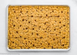 A baking sheet filled with evenly cut Egg-Free Sheet Pan Chocolate Chip Cookies, viewed from above on a light surface.