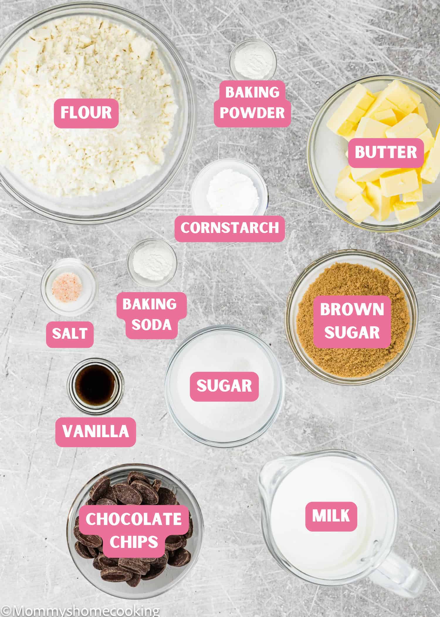 Overhead view of labeled baking ingredients in bowls and cups for Egg-Free Sheet Pan Chocolate Chip Cookies for a Crowd: flour, baking powder, butter, cornstarch, salt, baking soda, brown sugar, sugar, vanilla, chocolate chips, and milk.