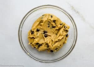 A glass bowl filled with eggless chocolate chip cookie ice cream cake dough on a light-colored surface.