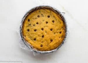 An Eggless Chocolate Chip Cookie Ice Cream Cake in a springform pan lined with plastic wrap, on a light surface.