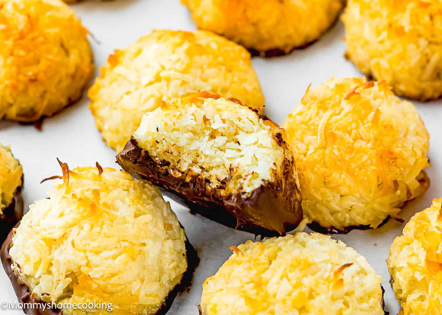 A close-up of Eggless Coconut Macaroons, some dipped in chocolate, with one macaroon broken in half to show the inside texture.