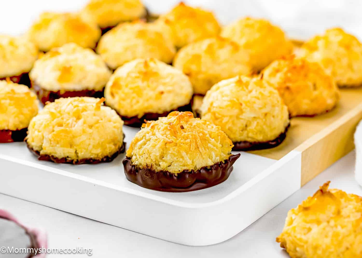 A tray of Eggless Coconut Macaroons, some with their bases dipped in chocolate, arranged on a white serving dish.