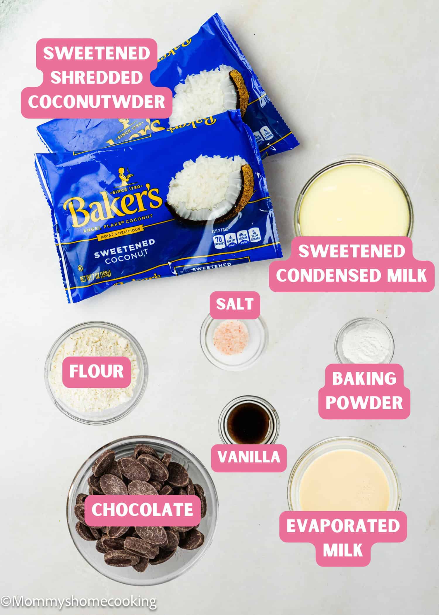 Various baking ingredients are arranged on a surface, including sweetened shredded coconut, chocolate, flour, salt, baking powder, vanilla, sweetened condensed milk, and evaporated milk—perfect for making Eggless Coconut Macaroons.