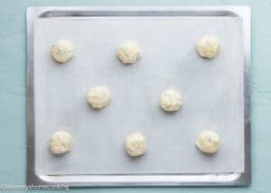 Nine unbaked Eggless Drop Sugar Cookies with Sprinkles are arranged on a parchment-lined baking sheet.