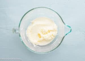 A glass mixing bowl with creamed butter and sugar for Eggless Drop Sugar Cookies with Sprinkles sits on a light blue surface.