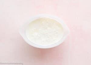 A white bowl filled with a frothy, creamy liquid sits on a light pink surface, perfect for pairing with Eggless Strawberry Pound Cake with Fresh Strawberries.