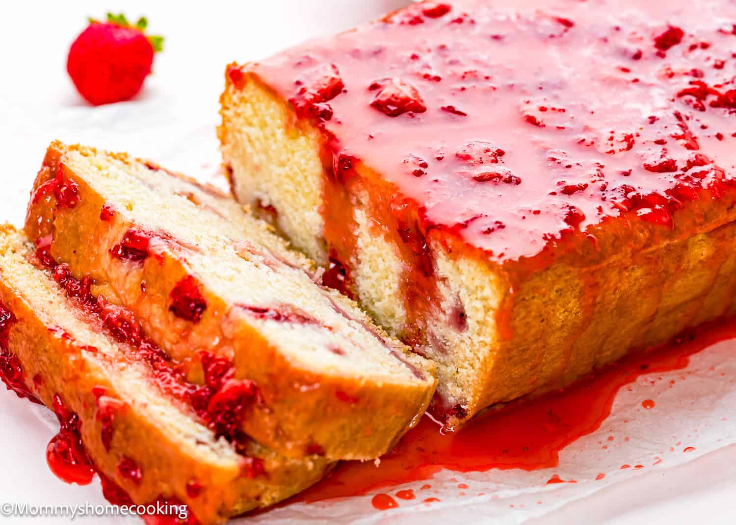 Eggless Strawberry Pound Cake with Fresh Strawberries, topped with a strawberry glaze and partially sliced, with a fresh strawberry in the background.