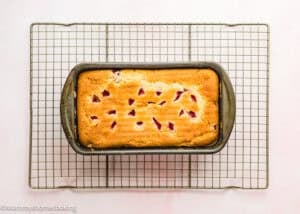 A rectangular loaf pan with Eggless Strawberry Pound Cake with Fresh Strawberries rests on a metal cooling rack over a light surface.