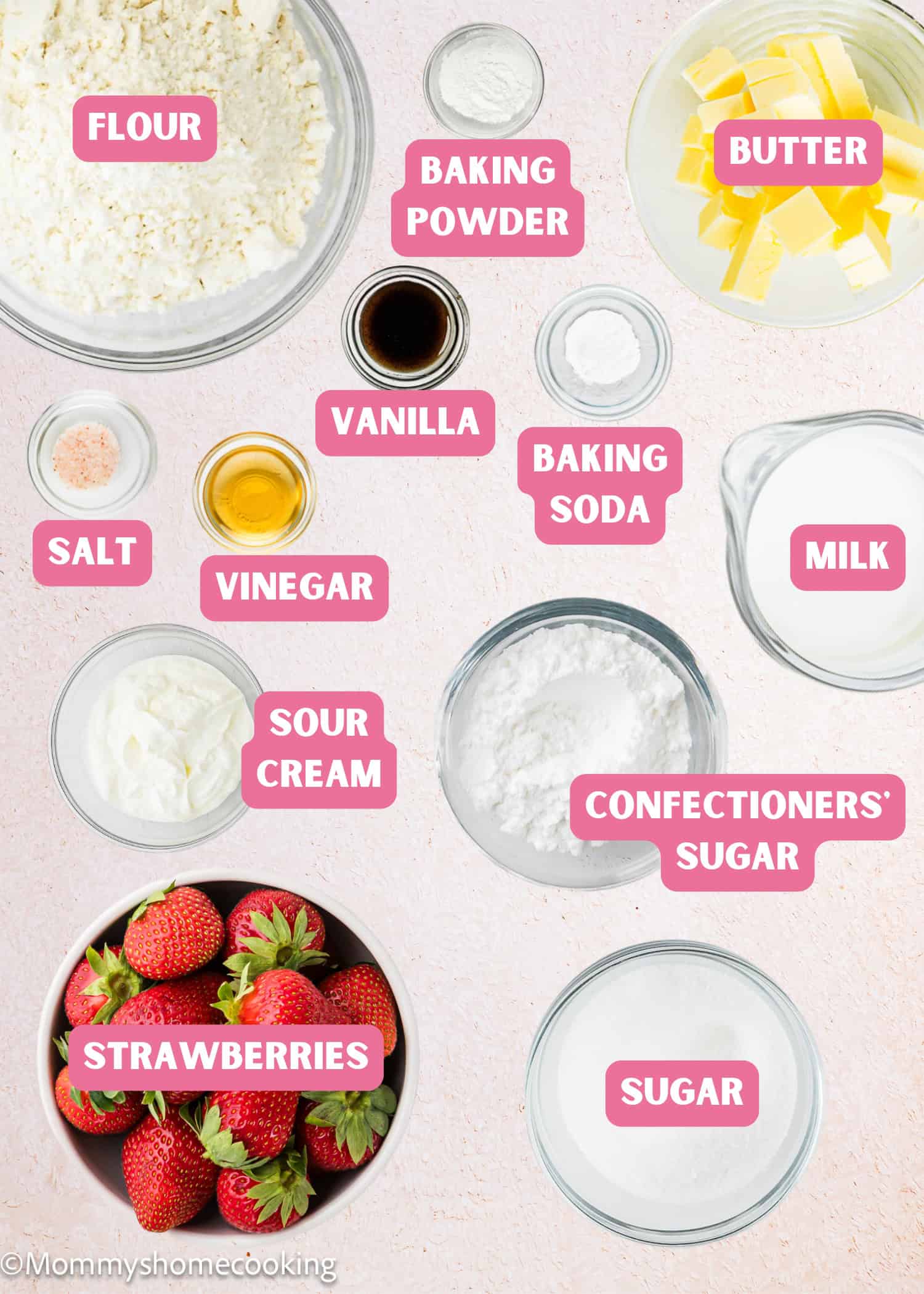 Various baking ingredients for Eggless Strawberry Pound Cake with Fresh Strawberries are arranged on a light surface, each labeled: flour, baking powder, butter, salt, vanilla, vinegar, baking soda, milk, sour cream, confectioners’ sugar, strawberries, and sugar.