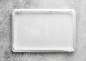 A rectangular baking sheet lined with parchment paper, placed on a scratched gray surface, ready for Eggless Brownie Ice Cream Sandwiches.