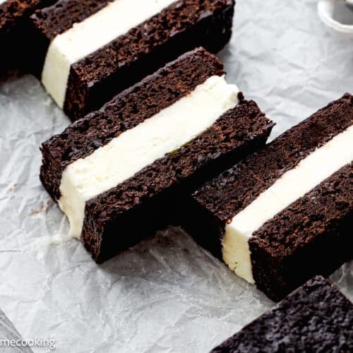 Three Eggless Brownie Ice Cream Sandwiches with white vanilla ice cream filling are arranged on crumpled parchment paper.