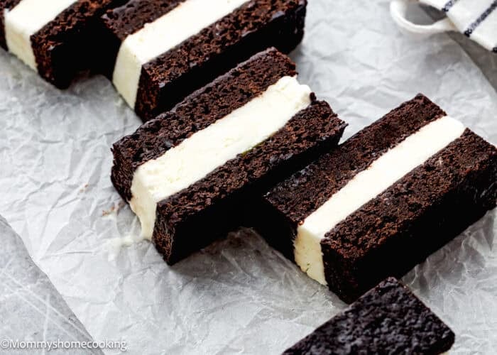 Three Eggless Brownie Ice Cream Sandwiches with white vanilla ice cream filling are arranged on crumpled parchment paper.