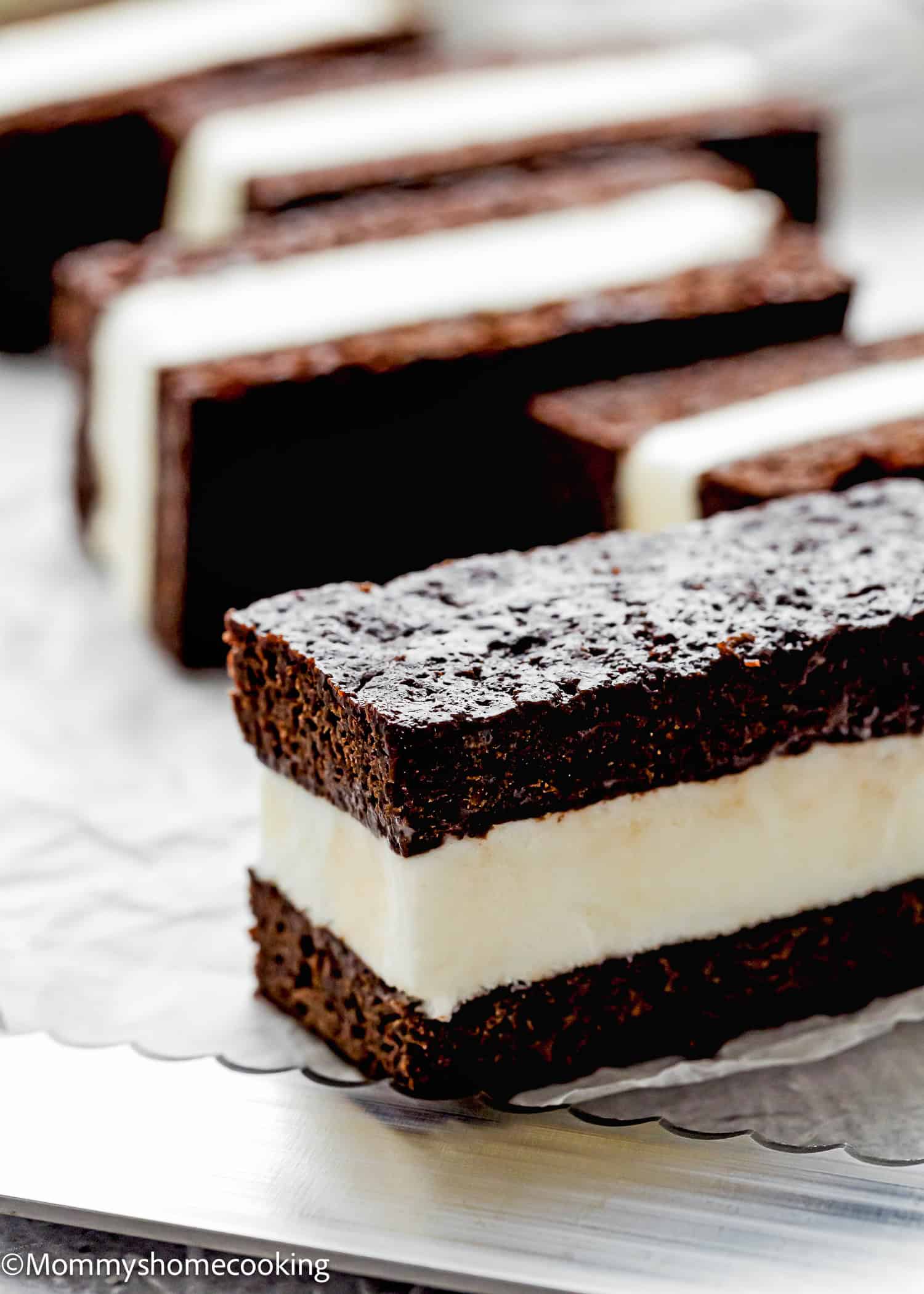 Eggless Brownie Ice Cream Sandwiches feature rectangular chocolate cake layers and a thick vanilla ice cream center, arranged in rows on a metal tray.