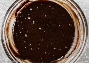 A glass bowl filled with thick, dark chocolate cake batter, partially mixed, with some batter clinging to the sides—perfect for making Eggless Brownie Ice Cream Sandwiches.