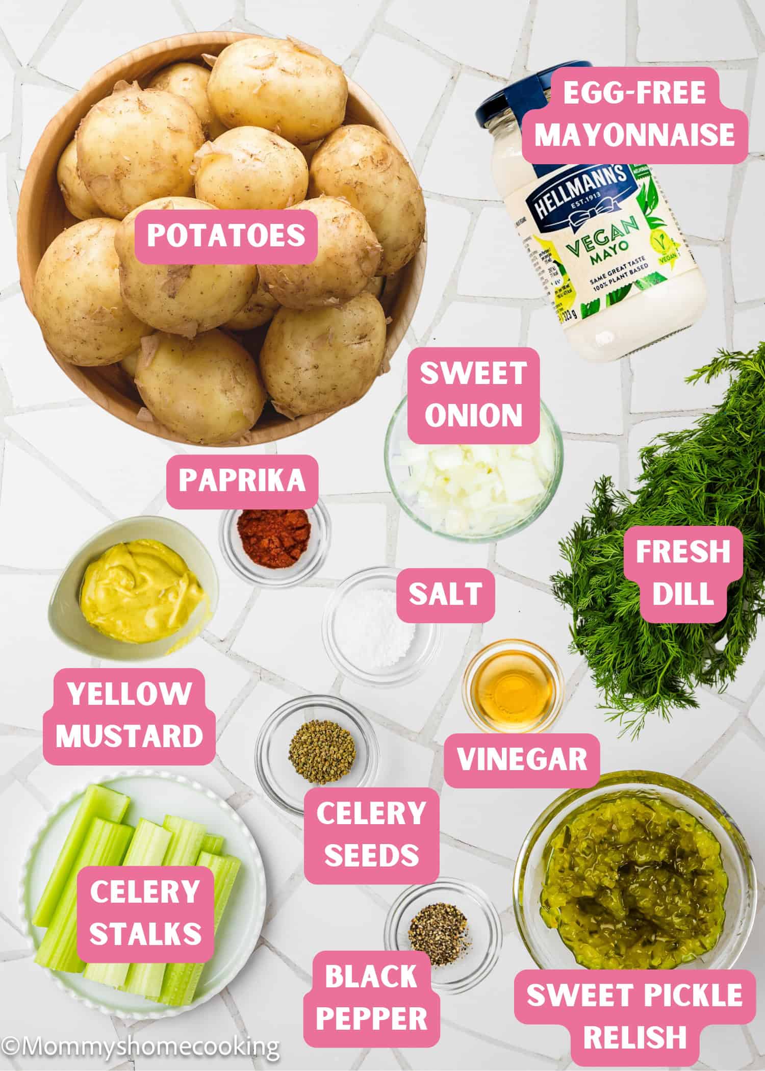 Ingredients for Egg-Free Potato Salad (Creamy Classic Recipe) are arranged on a white surface, including potatoes, egg-free mayonnaise, sweet onion, fresh dill, celery, vinegar, mustard, relish, paprika, salt, celery seeds, and pepper.