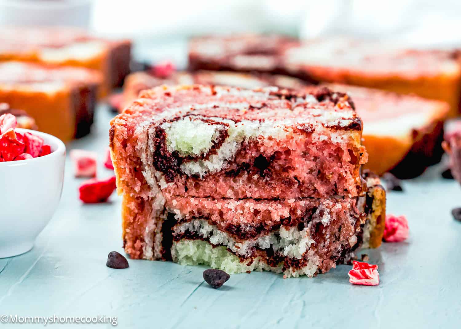 Close-up of two stacked slices of Eggless Neapolitan Loaf Cake with marbled chocolate and red bread, featuring chocolate chips and bits of red candy scattered nearby.