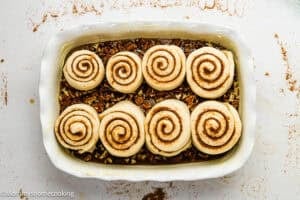 Eggless sticky buns arranged in a rectangular baking dish on top of chopped pecans, ready to be baked.