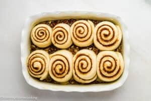 Eggless sticky buns arranged in a white rectangular baking dish on a light surface, ready to be baked.