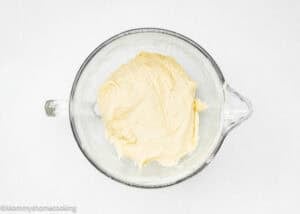 A glass mixing bowl filled with smooth, pale yellow Eggless Sticky Bun dough sits on a white surface.