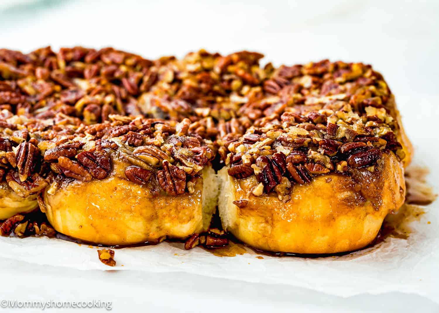 Close-up of Eggless Sticky Buns topped with chopped pecans on parchment paper, with one roll partially separated from the rest.