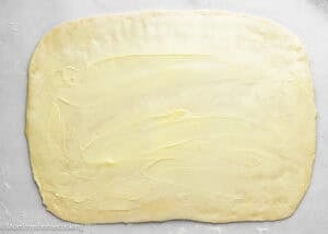 Rectangular sheet of dough rolled out on a light surface with an even layer of butter spread across the top, perfect for making Eggless Sticky Buns.