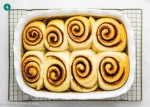 A rectangular white baking dish with seven eggless sticky buns placed on a wire cooling rack.