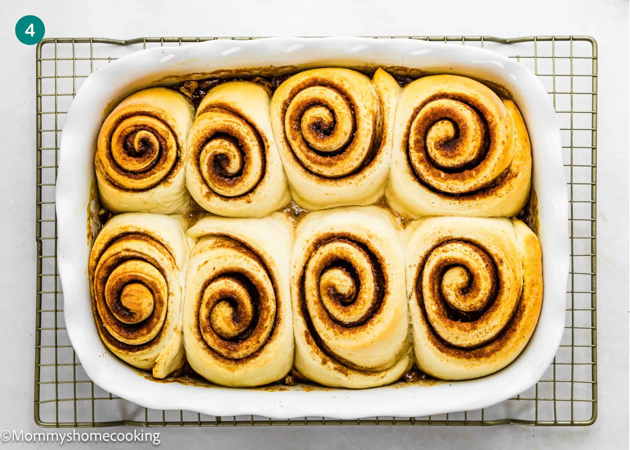 A rectangular white baking dish with seven eggless sticky buns placed on a wire cooling rack.