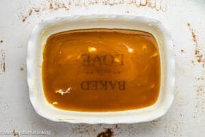 A white ceramic dish filled with caramel sauce; the words “BAKED WITH LOVE” are faintly visible through the sauce at the bottom, perfect for serving Eggless Sticky Buns.