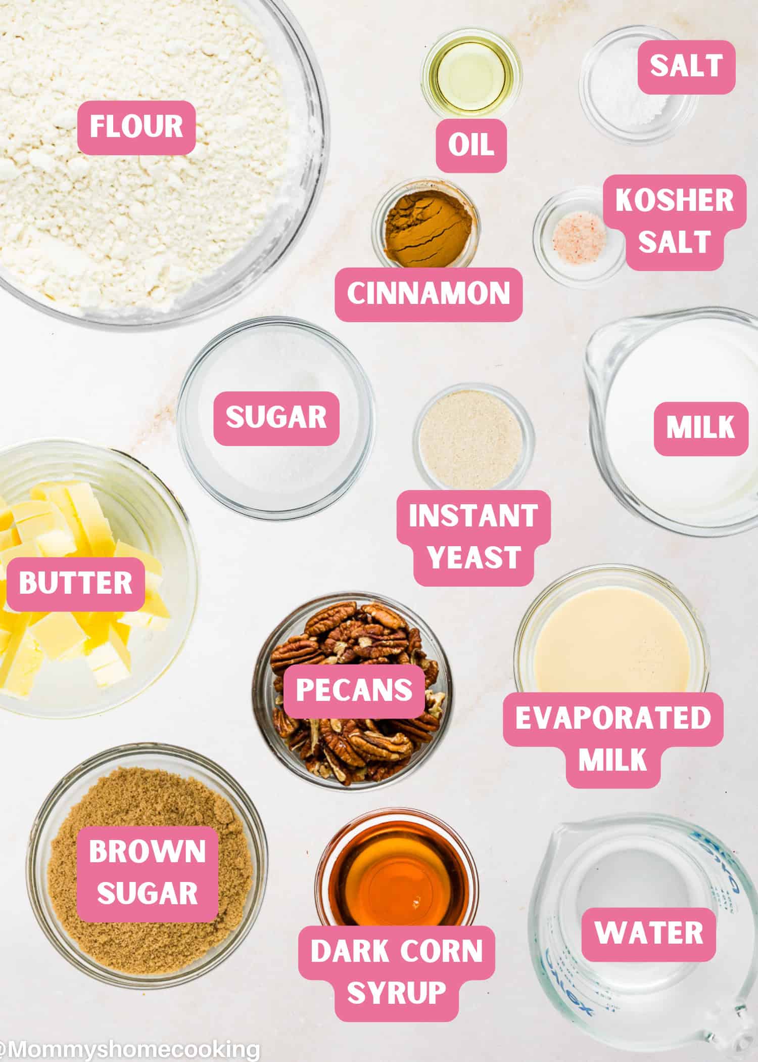 Assorted baking ingredients in labeled bowls, including flour, sugar, milk, butter, brown sugar, pecans, cinnamon, instant yeast, evaporated milk, oil, water, salt, and dark corn syrup—perfect for making Eggless Sticky Buns.