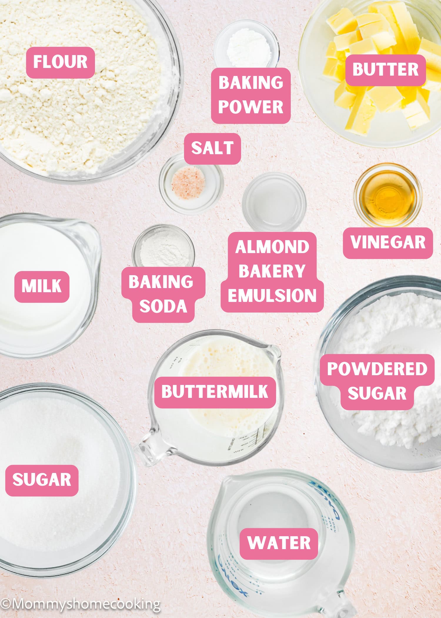 Top-down view of labeled baking ingredients in glass bowls, showcasing everything you need to make an Eggless White Texas Sheet Cake—flour, butter, sugar, milk, buttermilk, baking powder, baking soda, salt, vinegar, water, almond emulsion, and powdered sugar.