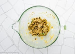 A glass mixing bowl containing Peanut-Free Monster Cookie Protein Energy Bites dough sits on a white tiled surface.