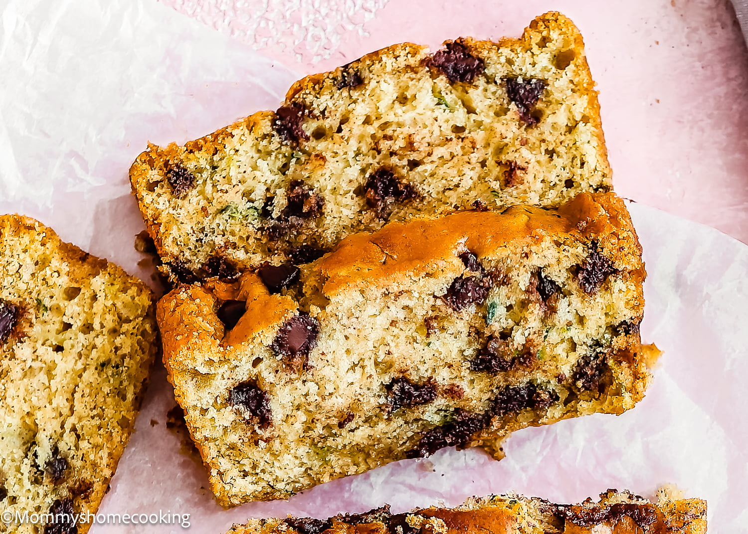 Three slices of Eggless Chocolate Chip Zucchini Bread on parchment paper, shown from above.